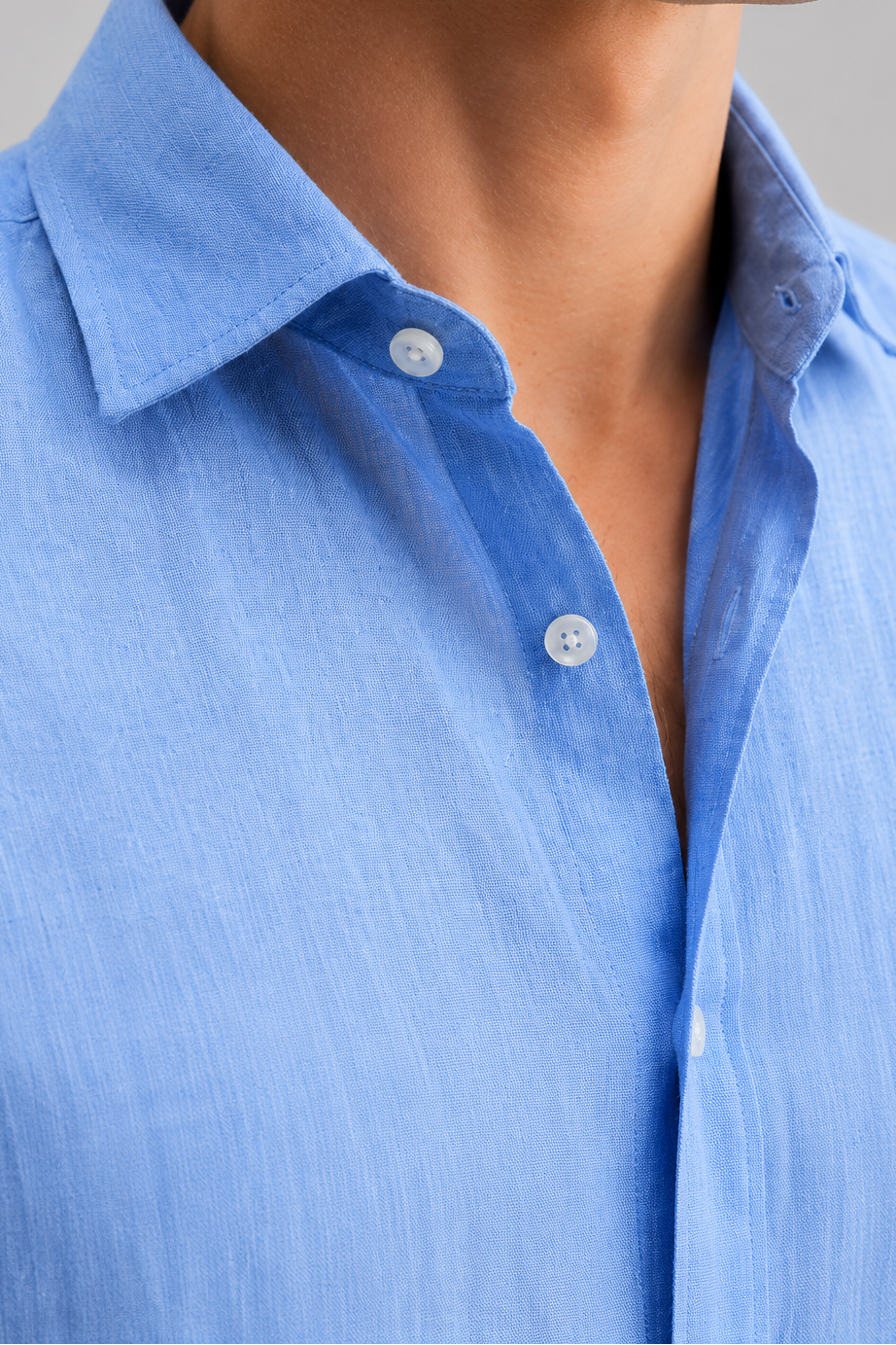 Close-up of a person wearing a blue button-up shirt with a neutral background