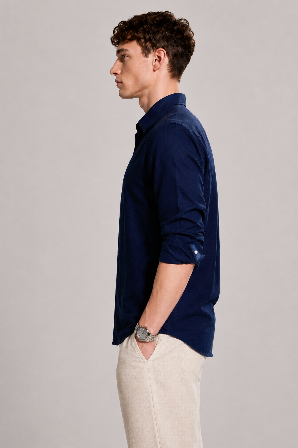 Man wearing a navy blue shirt and beige pants against a plain background